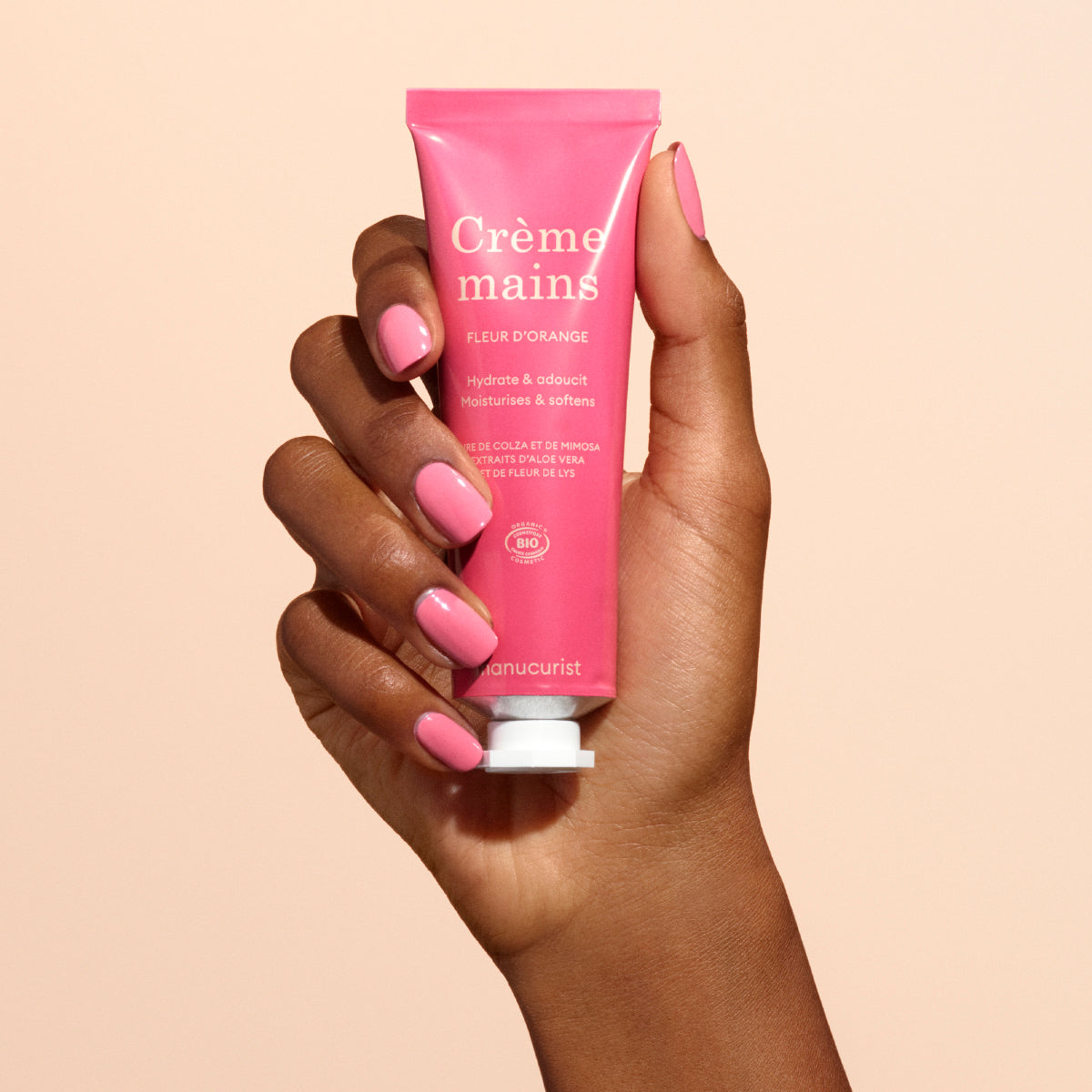 A hand with pink nails holds a pink tube of Manucurist Fleur d&