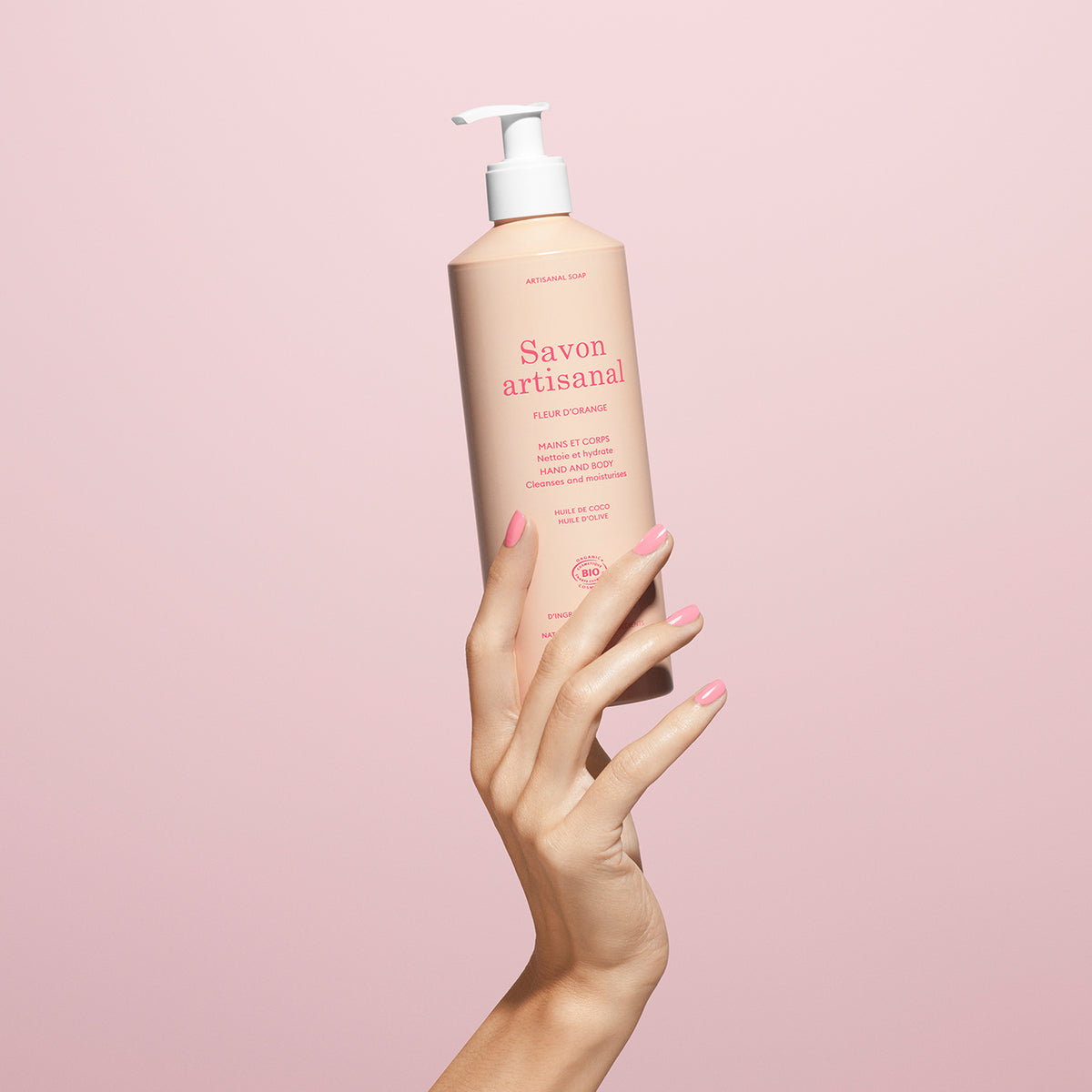 A hand with pink nails holds a 500ml Manucurist Fleur d&