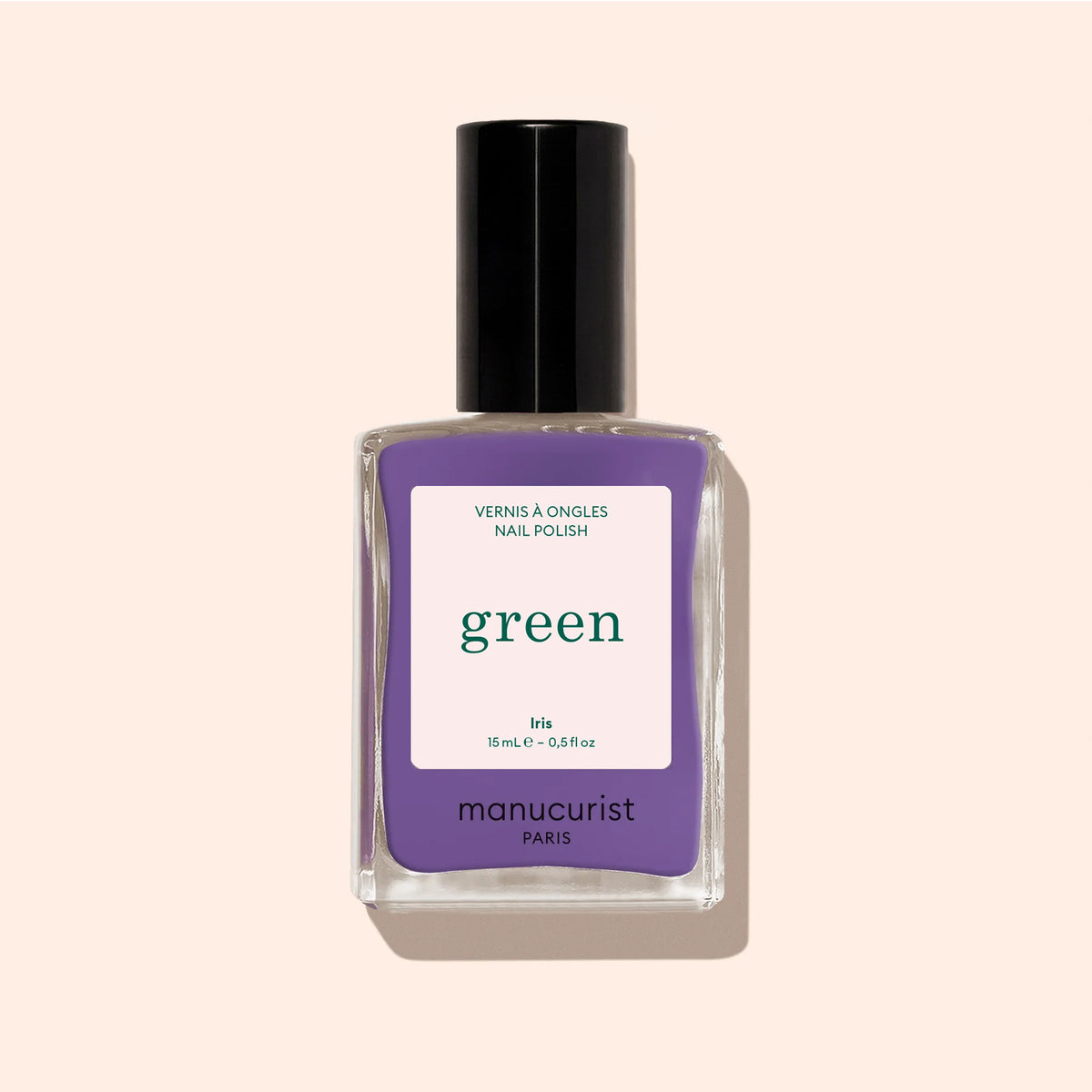 A bottle of Manucurist Iris nail polish, a purple shade with blue undertones from the Green™ range, featuring a black cap and displayed against a light beige background.
