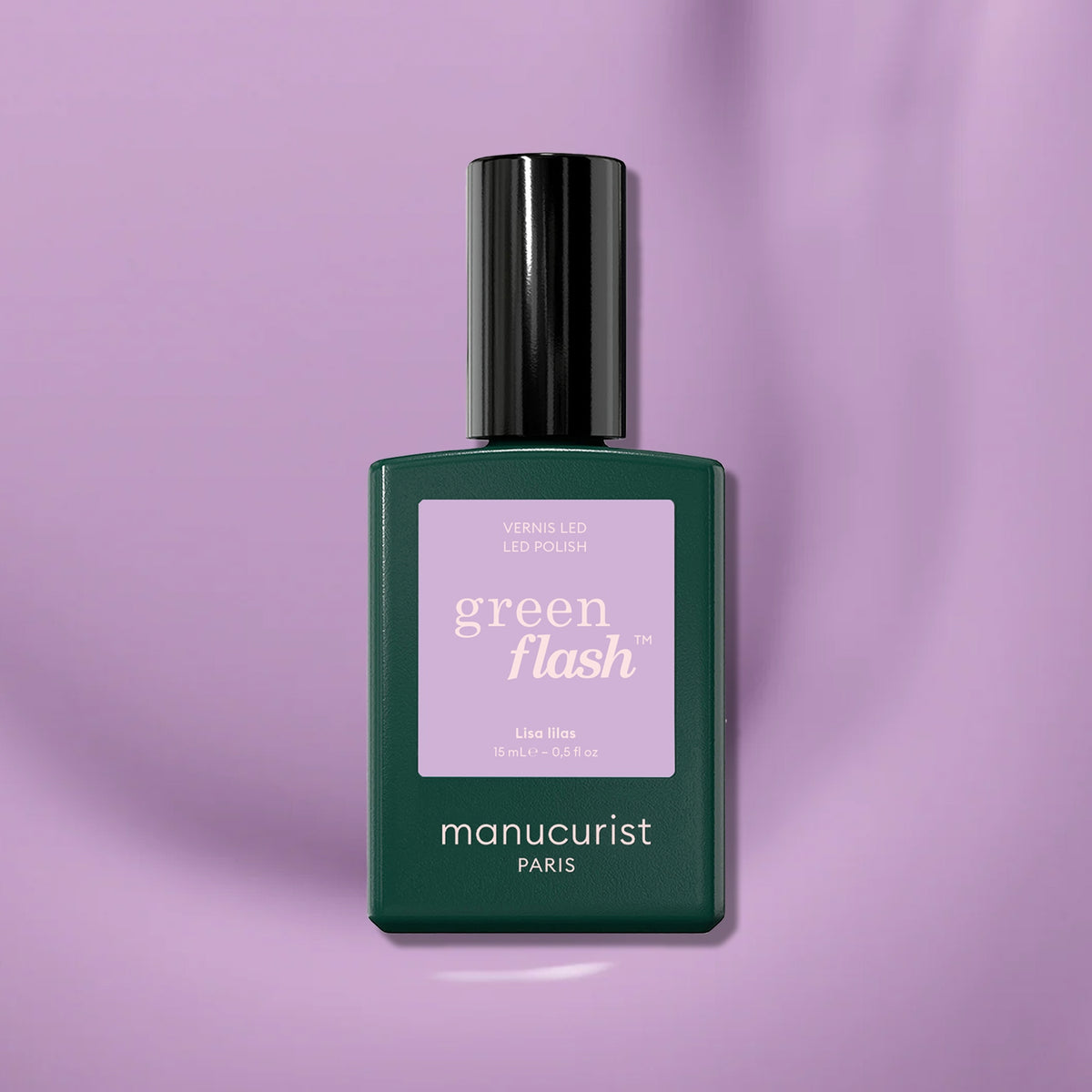 A chic bottle of Manucurist Lisa Lilas gel polish rests on a shiny, light purple surface. The dark green bottle with black cap and lilac label highlights this elegant lilac shade from Manucurist.