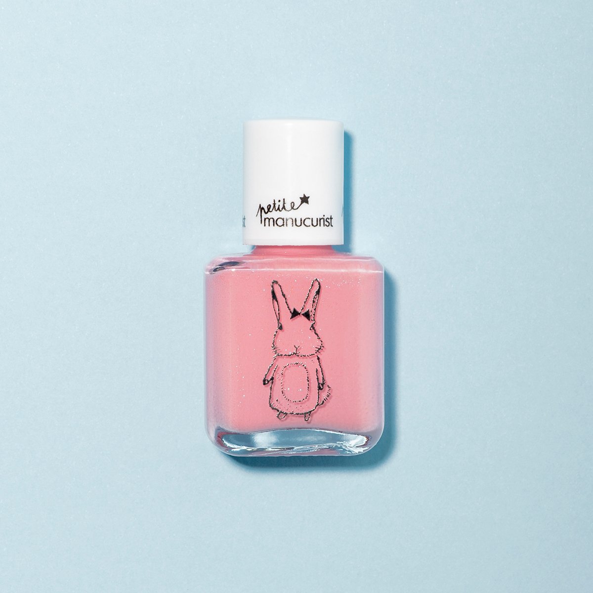 A bottle of Manucurist "Rosie the Rabbit" pink kids nail polish with a white cap labeled "petit manucurist" and a black bunny illustration, shown against a light blue background.