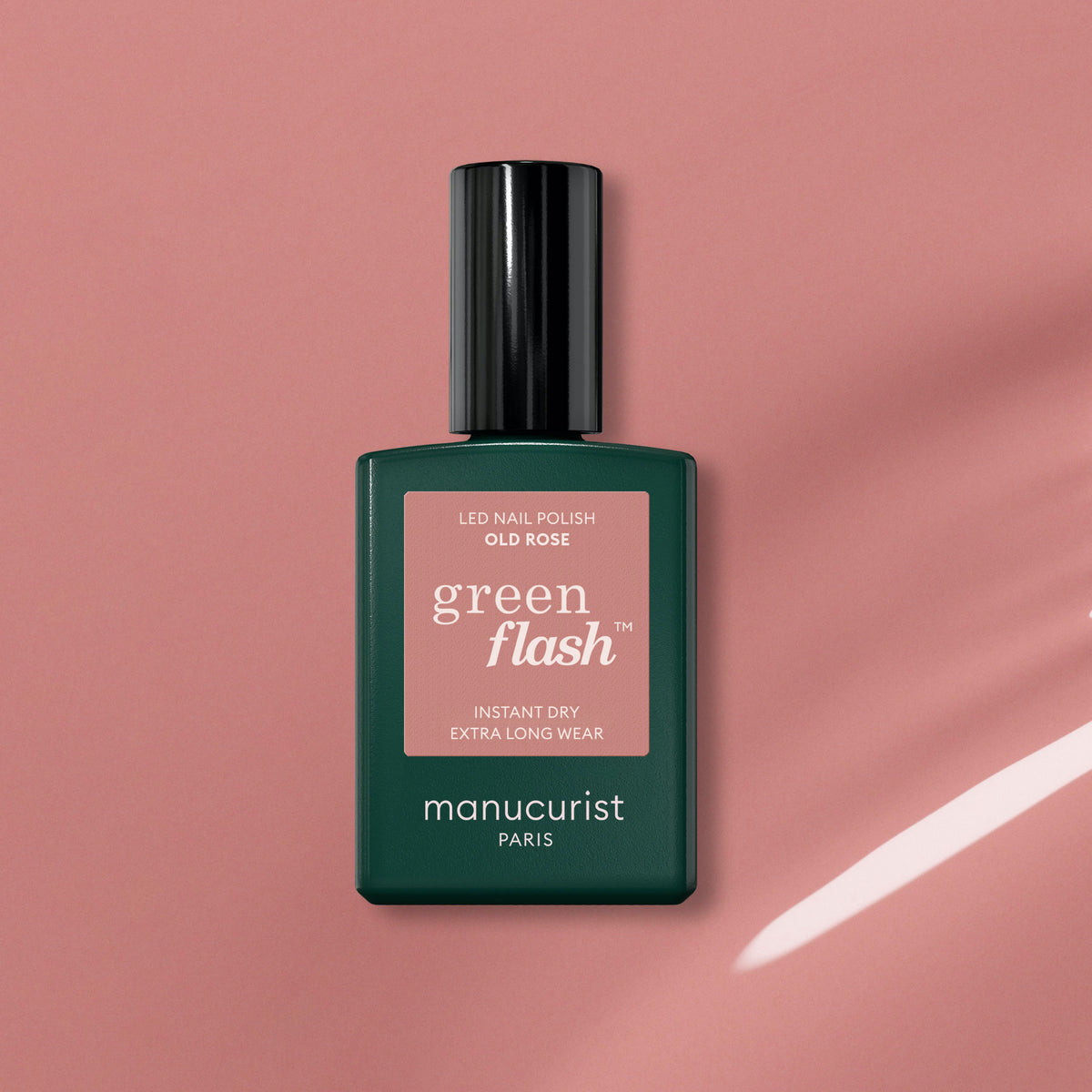 A bottle of Manucurist Old Rose gel polish—an antique pink shade—rests on a pink background, its dark green cap and label reflecting the light.