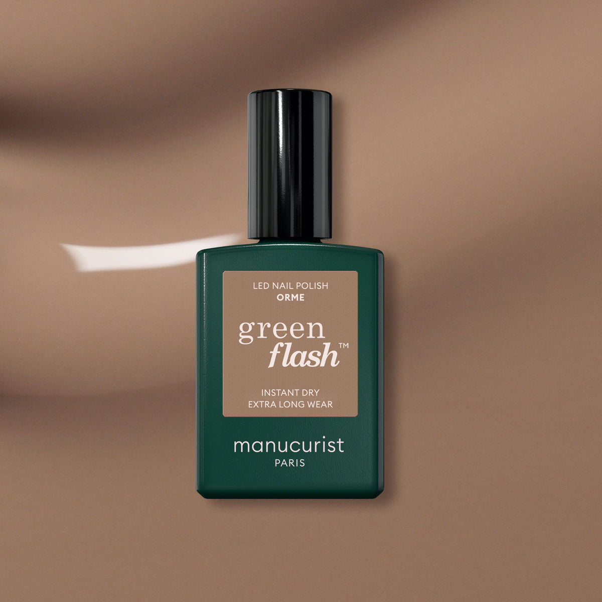 A bottle of Manucurist Orme Green Flash gel polish rests on a brown background, displaying its rectangular shape with a dark green label and black cap—perfect for anyone seeking an eco-friendly manicure.