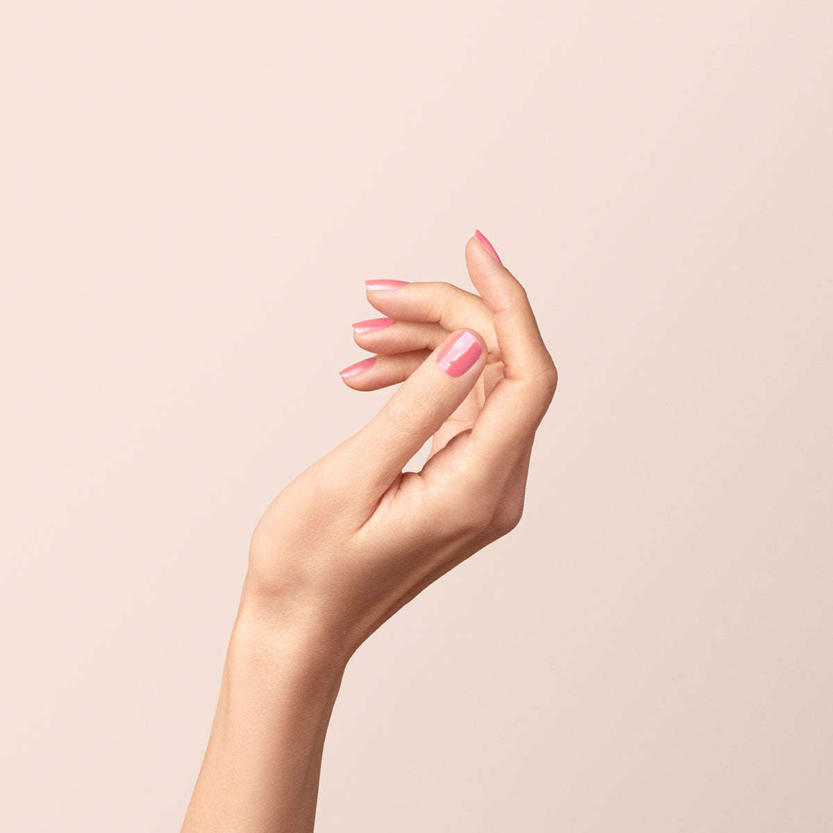 A hand with light skin is elegantly posed against a pale beige background, showcasing neatly manicured nails painted with Manucurist&