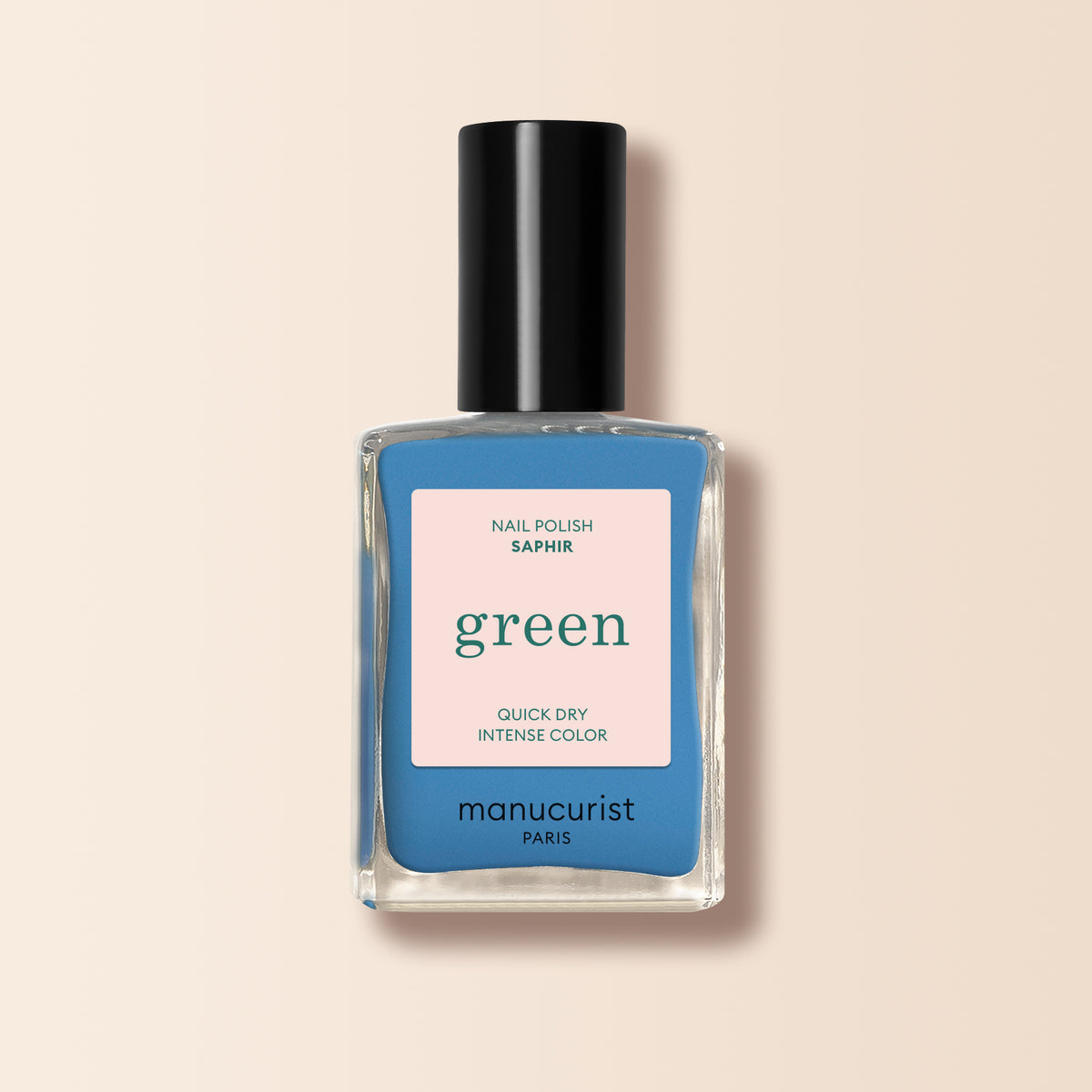 Manucurist’s Saphir nail polish, a jewel-toned azure blue with a black cap and beige label, stands out against the light beige background.