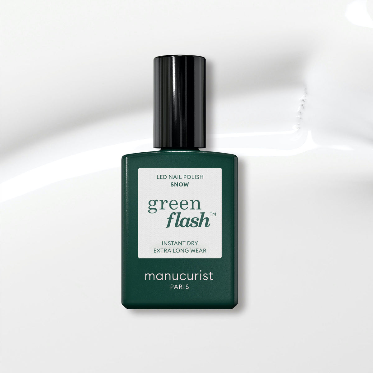A dark green Manucurist bottle of Green Flash gel polish in the shade Snow, labeled as instant dry and extra long wear, sits on a glossy white surface—an ideal pure white nail polish option.