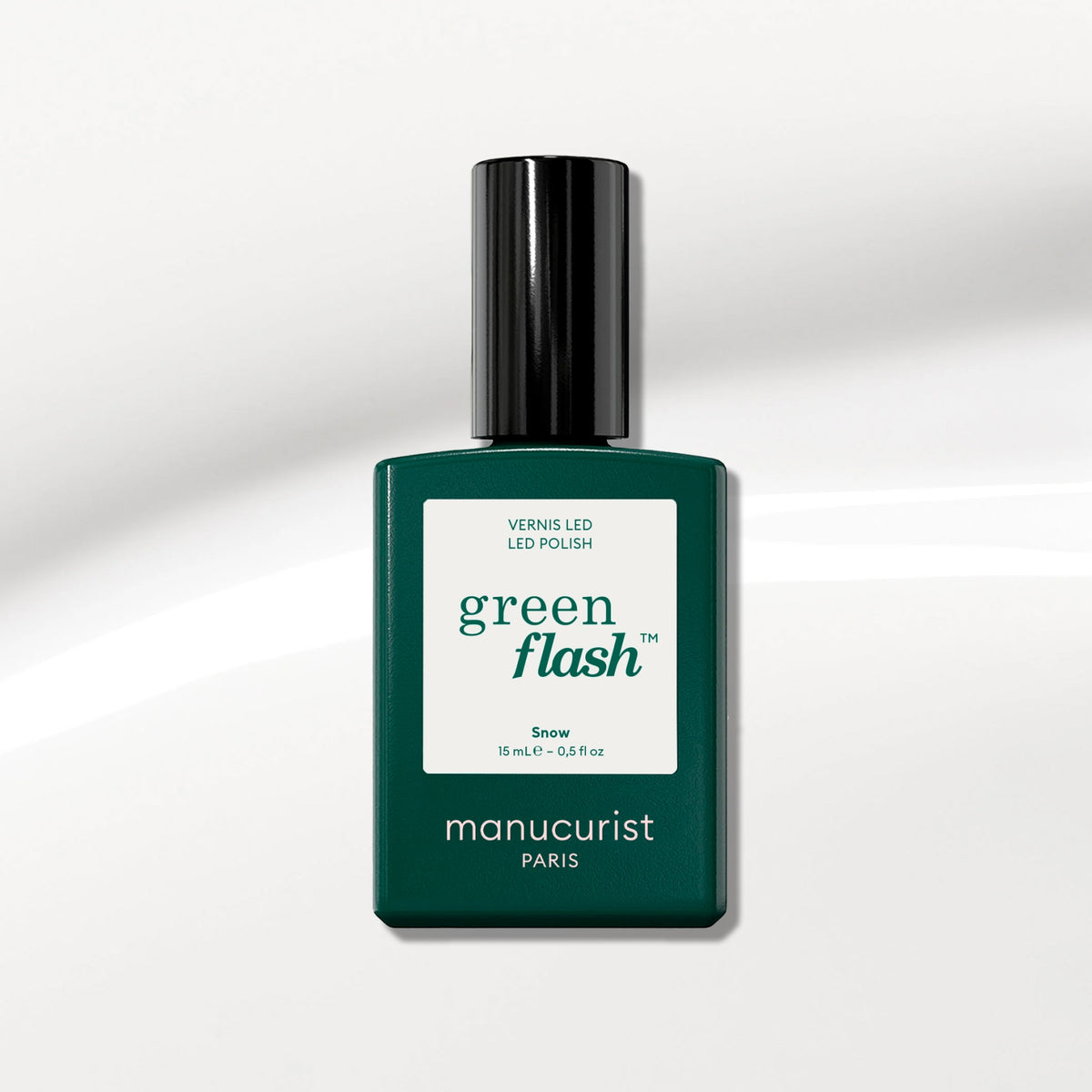 A dark green Manucurist bottle of Green Flash gel polish in the shade Snow, labeled as instant dry and extra long wear, sits on a glossy white surface—an ideal pure white nail polish option.