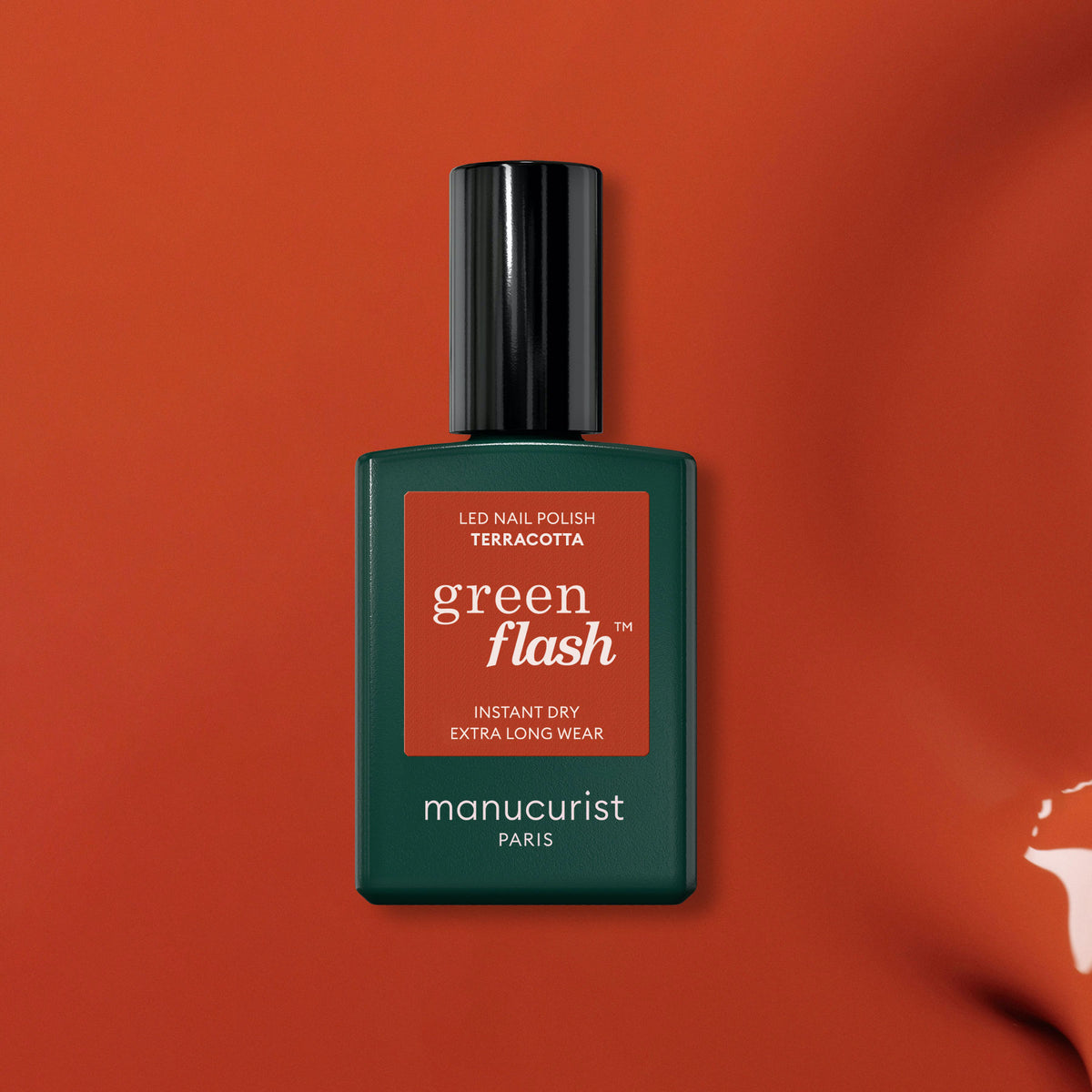 A green rectangular bottle of Manucurist gel polish in the shade Terracotta is shown on a burnt orange background, with a black cap and white text, evoking the warmth of scorched red earth.