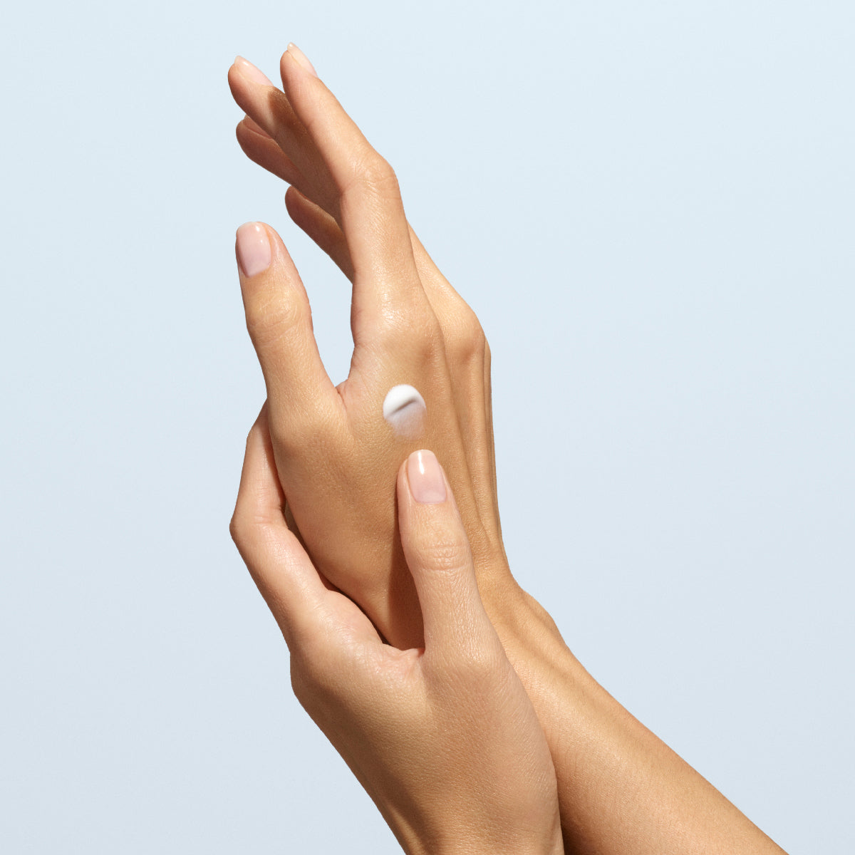A close-up of neatly manicured hands; one applies a dab of Manucurist Lavande Vraie Hand Cream - Cosmos Organic to the back of the other, set against a plain, light background.