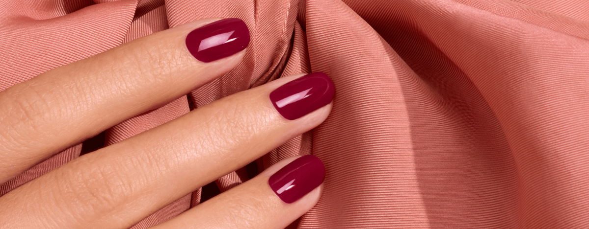 Hand with fingernails painted a glossy dark red against draped, peachy-pink fabric.