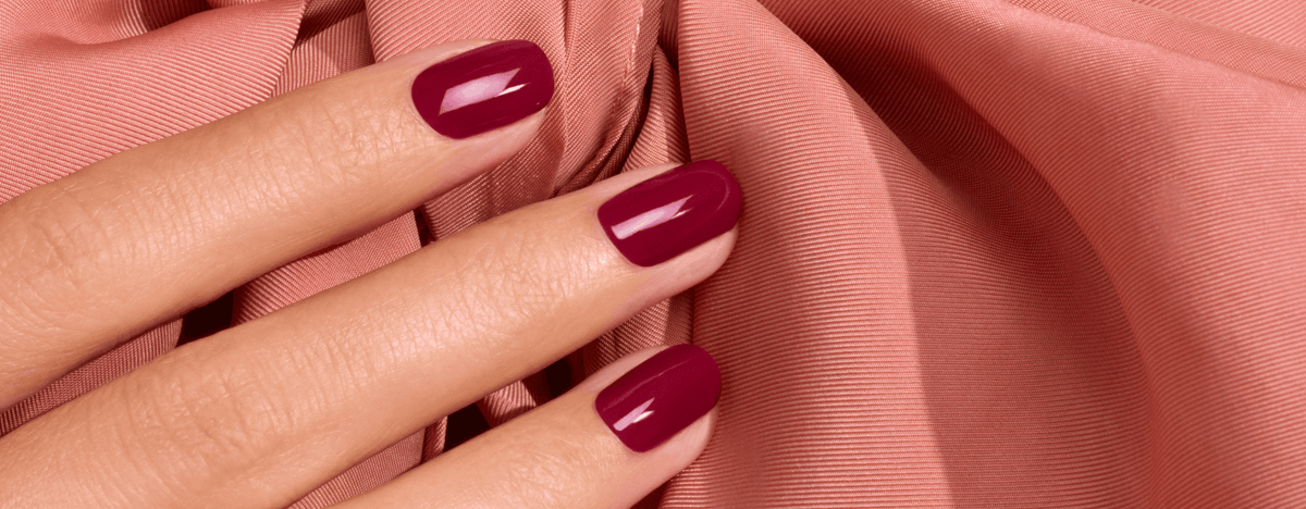 A hand with dark red nail polish resting on draped peach fabric.