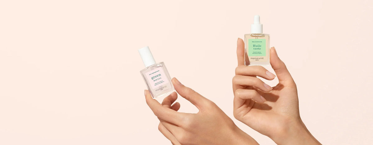 Two hands holding skincare bottles against a plain beige background. One bottle is labeled Serum, the other has a dropper and is labeled Huile Verte. Both labels are light-colored.