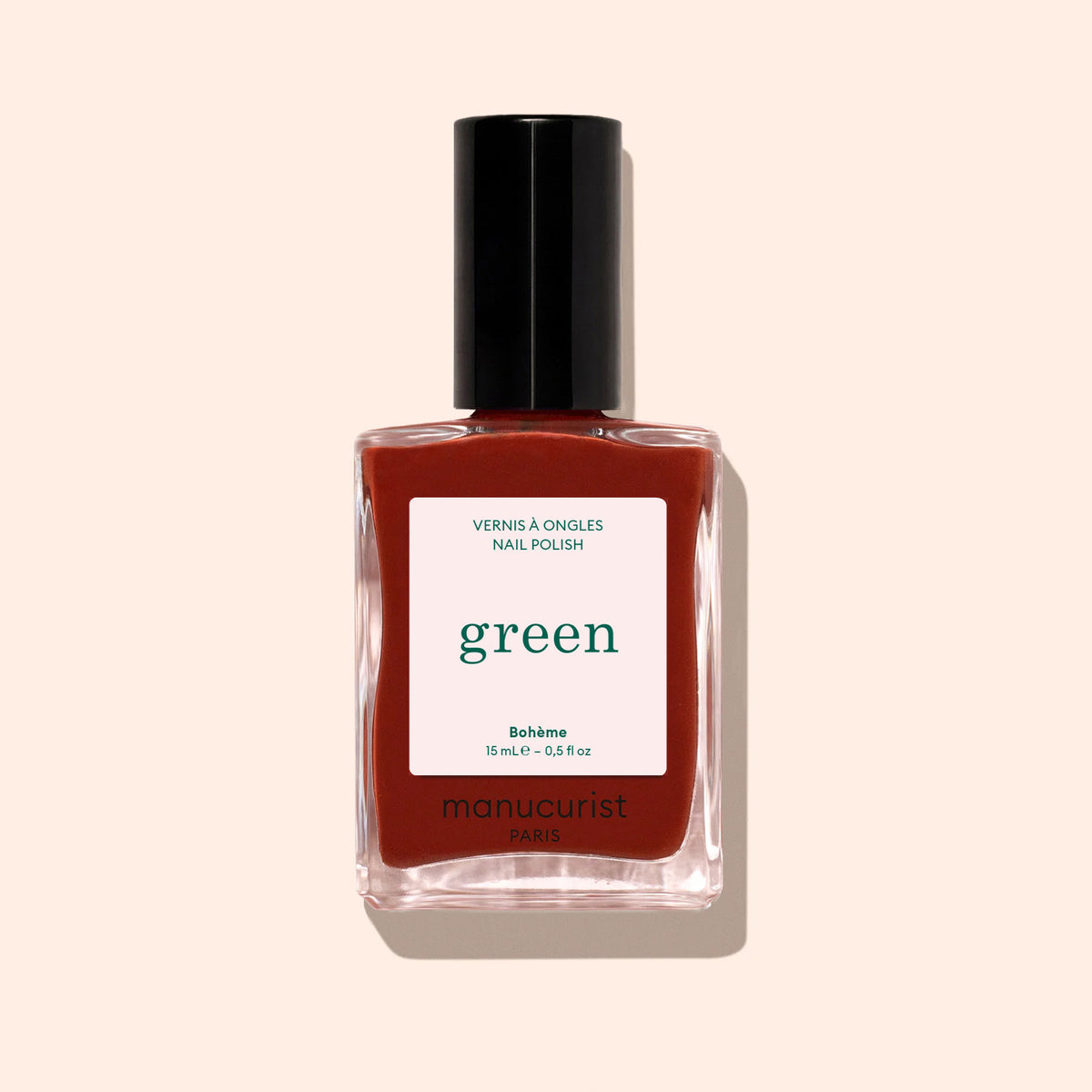 A bottle of Manucurist Bohème red-brown nail polish with a black cap, labeled green and quick dry intense color, set on a light beige background—ideal for those seeking Montmartre-inspired style.