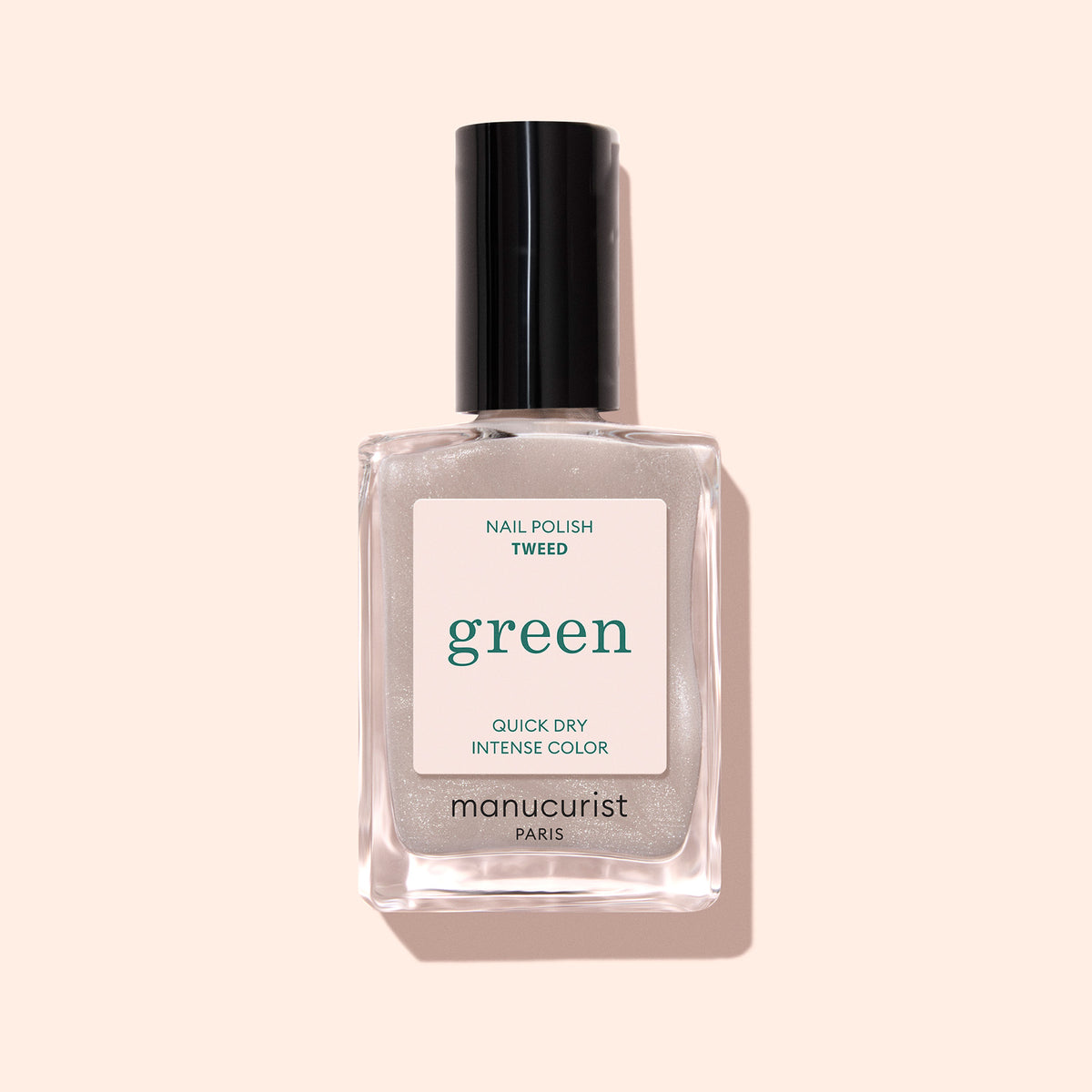 A bottle of Manucurist Tweed nail polish, from the Green line, features chic grey polish with a pearly sheen in a clear rectangular bottle with a black cap and white label, set against a light beige background.