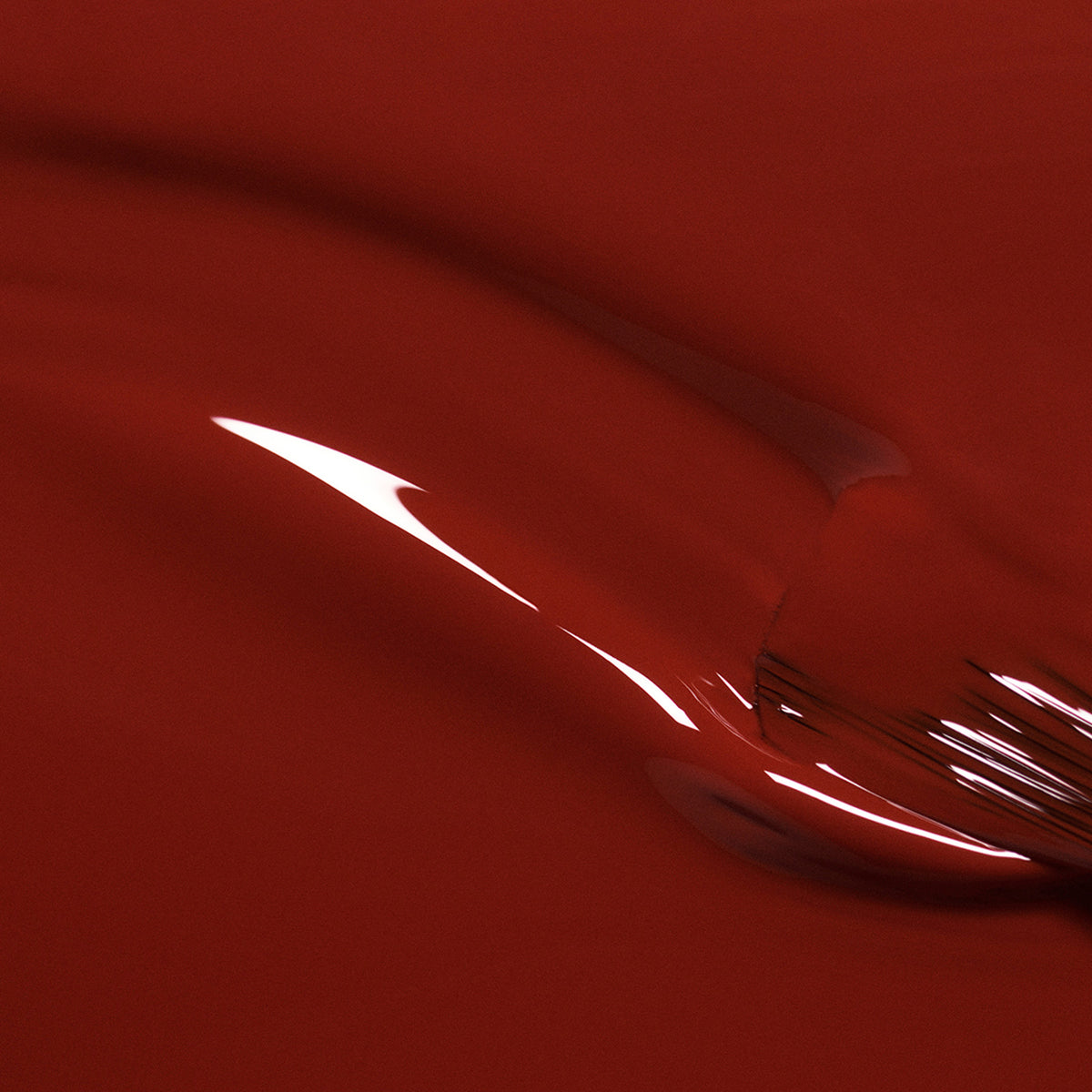 A close-up of Manucurist’s Bohème nail polish reveals glossy red-brown hues with smooth, flowing curves and reflective highlights, creating an abstract, shiny surface full of movement.