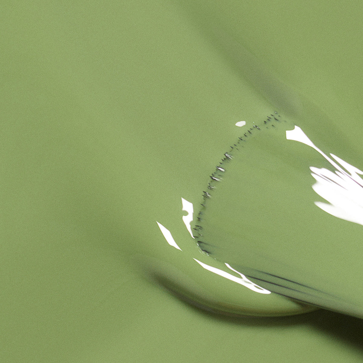 A close-up of Manucurist’s Tuileries, a glossy olive green polish, is smoothly applied with a flat tool, forming soft curves and gentle reflections reminiscent of Paris gardens.