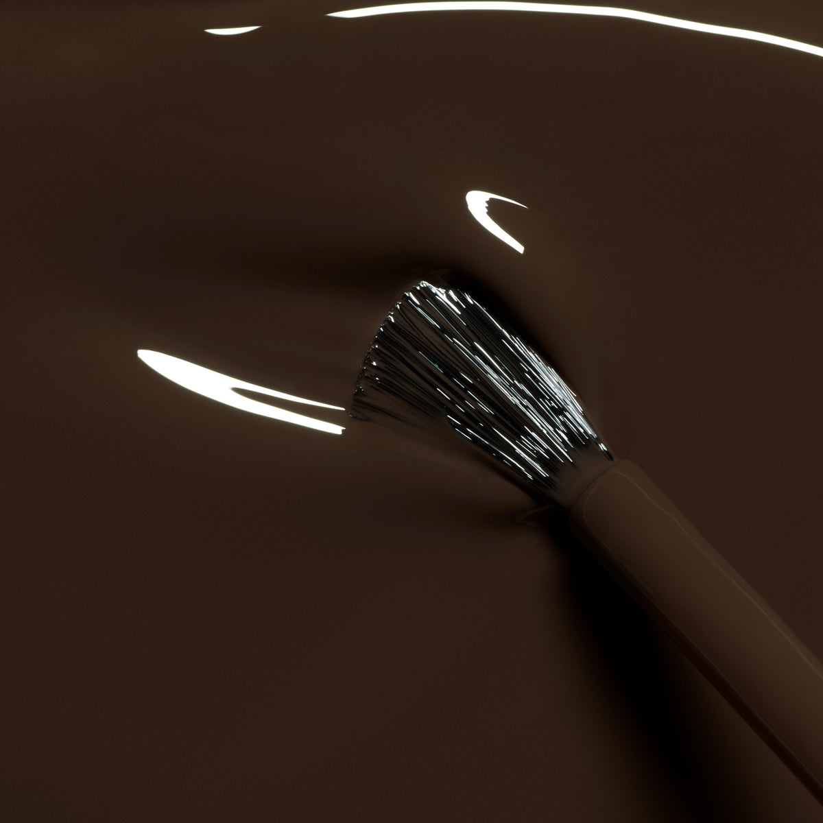 A close-up of a makeup brush with black and white bristles, partially dipped in Manucurist&