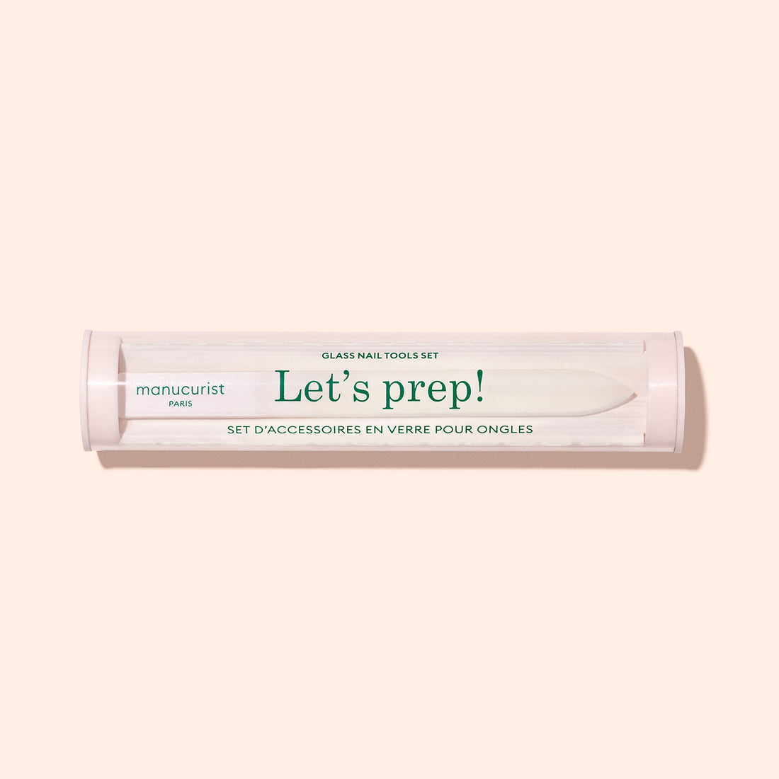 A clear cylindrical container labeled "Glass nail accessory trio" by Manucurist, designed to hold glass nail tools, is displayed against a light beige background.
