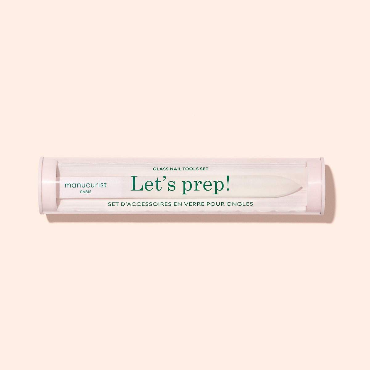 A clear cylindrical container labeled "Glass nail accessory trio" by Manucurist, designed to hold glass nail tools, is displayed against a light beige background.