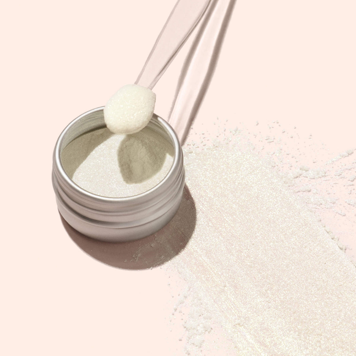 An open jar of Manucurist Golden Glazed Powder, a shimmery white manicure powder, sits on a pale background with pearly gold powder beside it and a spatula scooping some out.