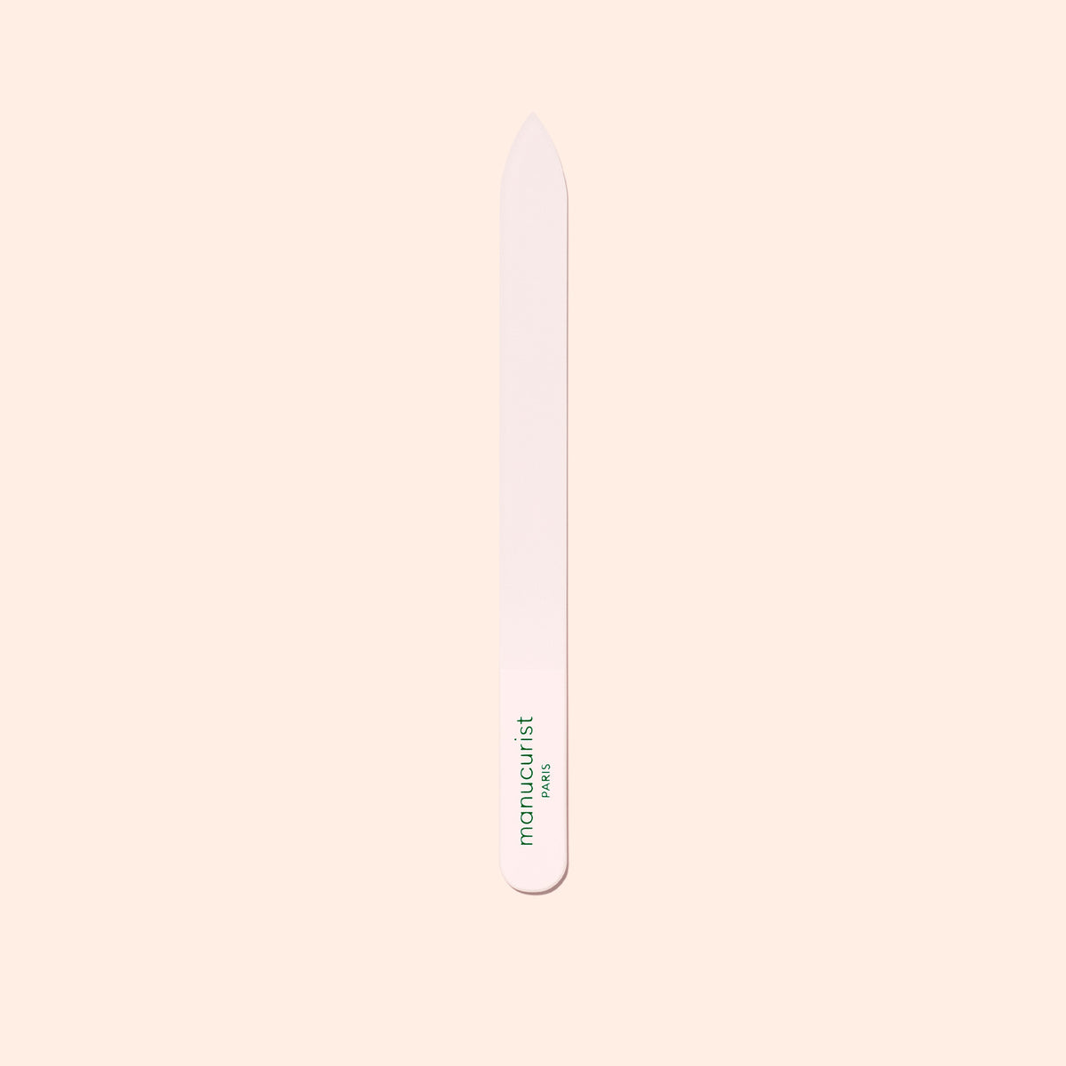 A Manucurist Glass Nail File with rounded edges and "manucurist" in green lettering stands vertically against a pale beige background.