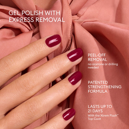 A hand with short, glossy, dark pink gel-polished nails featuring Manucurist’s Advent Calendar Time to Flash! rests on pink fabric. Text highlights include easy peel-off removal, a patented strengthening formula, and up to 21 days of wear when used with the special top coat—perfect for creating a long-lasting gel polish manicure under an LED lamp.