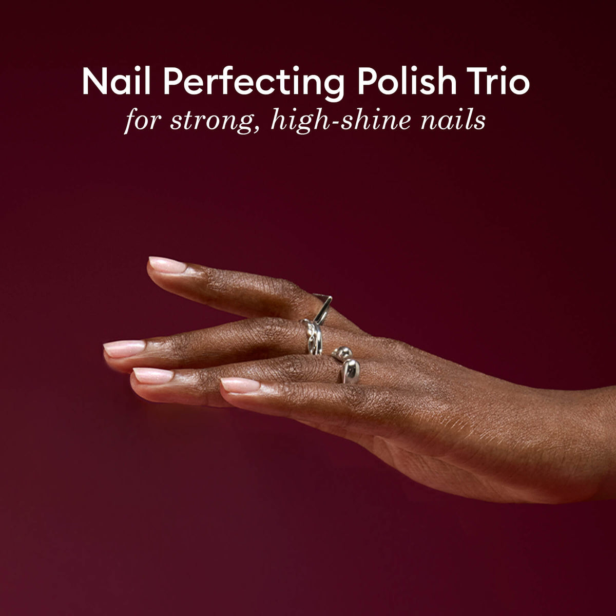 A hand with polished nails and silver rings appears against a deep burgundy backdrop. Above, text reads: Manucurist Active Icons Trio—an exclusive nail care set for strong, glossy nails.