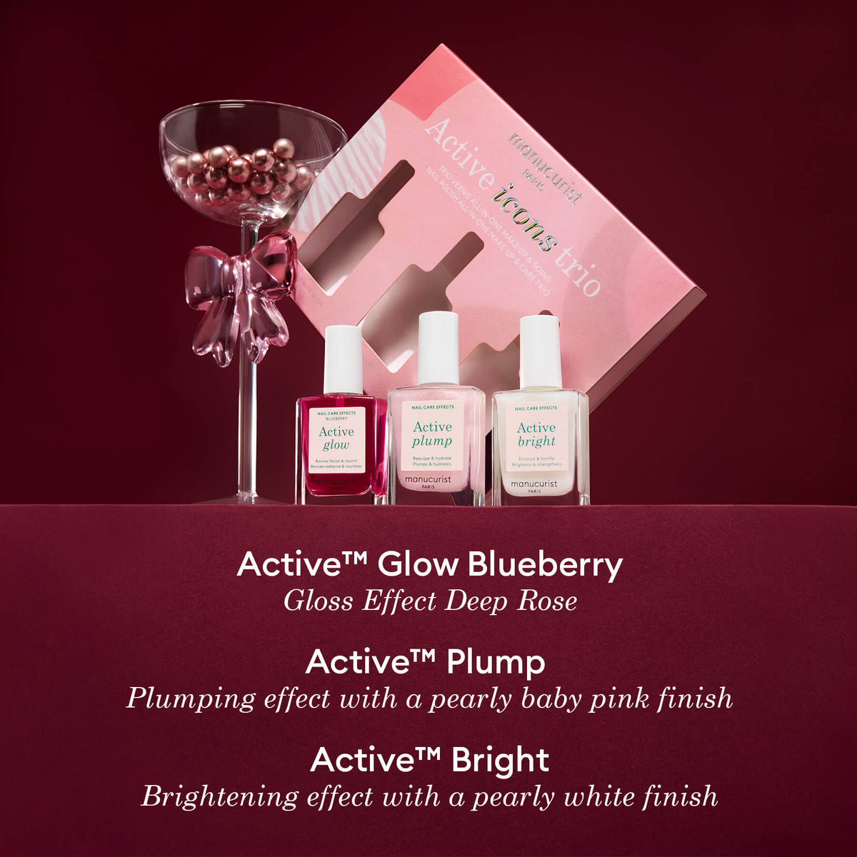 A pink and wine-themed display showcases Manucurist’s limited edition Active Icons Trio—three nail care bottles (Glow, Plump, Bright)—with a martini glass of pearls and a pink gift box, making it the perfect nail polish gift set.