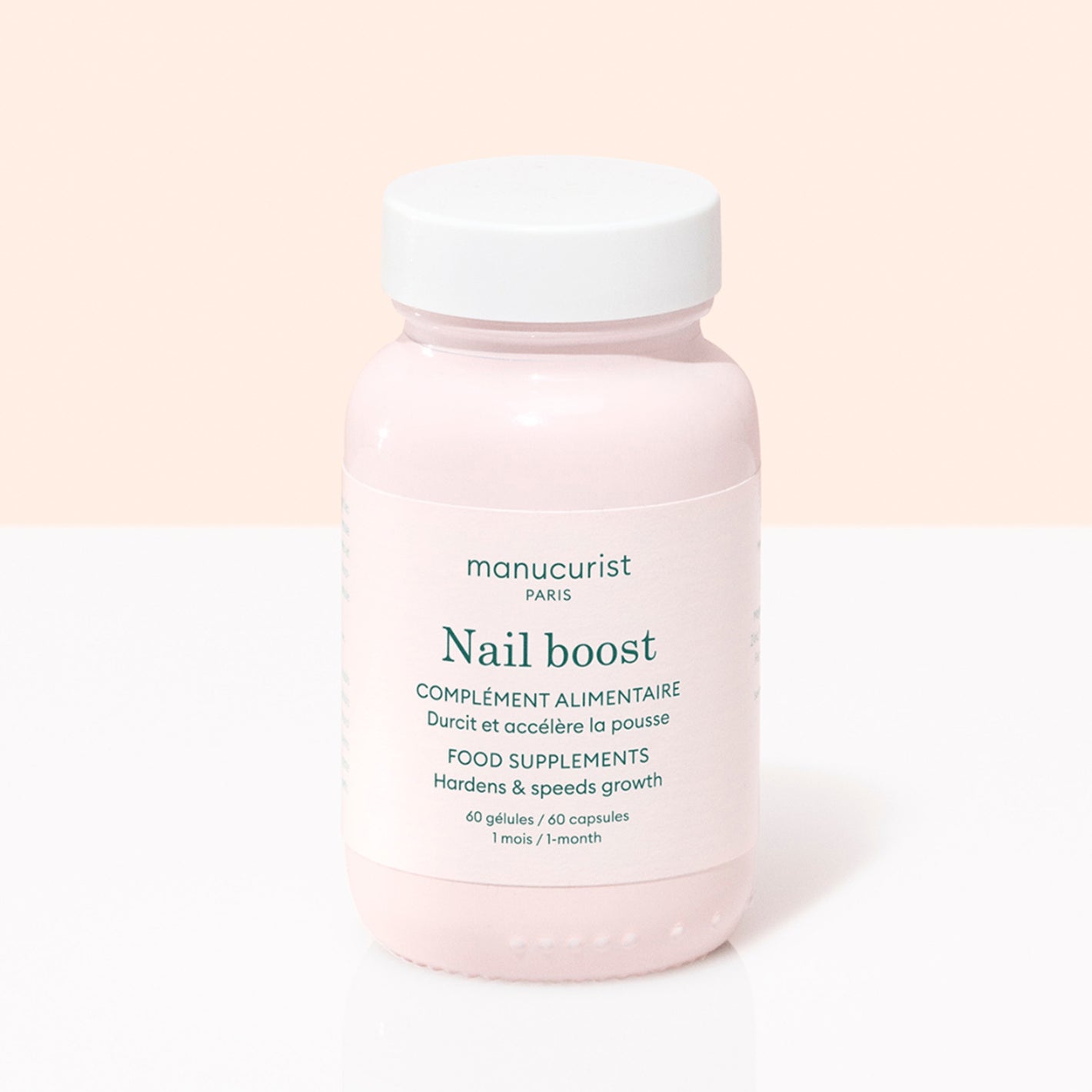 A pink Manucurist Nail Boost bottle, a nail supplement with 60 capsules for one month’s use to strengthen nails and boost growth, is shown against a light two-tone background.