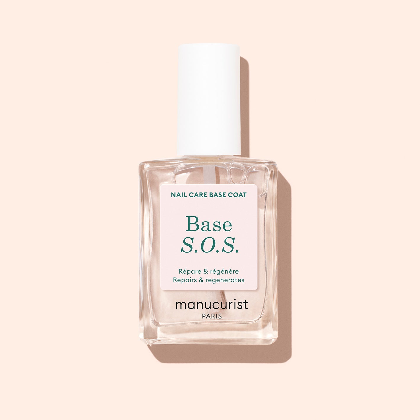 A clear bottle of Manucurist S.O.S Nail Strengthener with a white cap is displayed upright on a light beige background. The bilingual label suits anyone seeking effective nail repair and care for damaged nails.