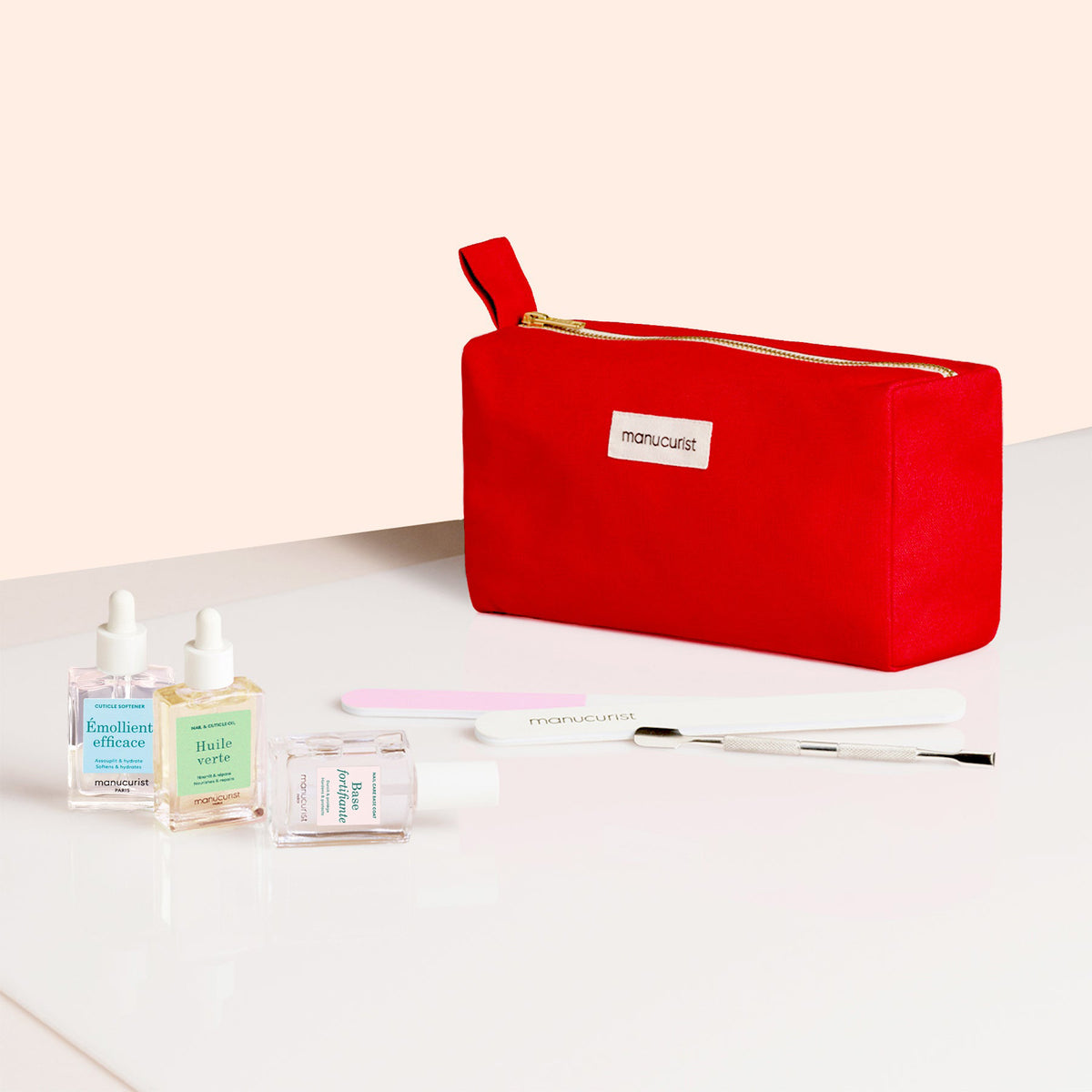 The Complete Nail Care Kit by Manucurist is shown in a red zippered pouch, featuring three nail care liquids, a nail file, cuticle remover, cuticle pusher, and brush on a white surface with a light beige background.
