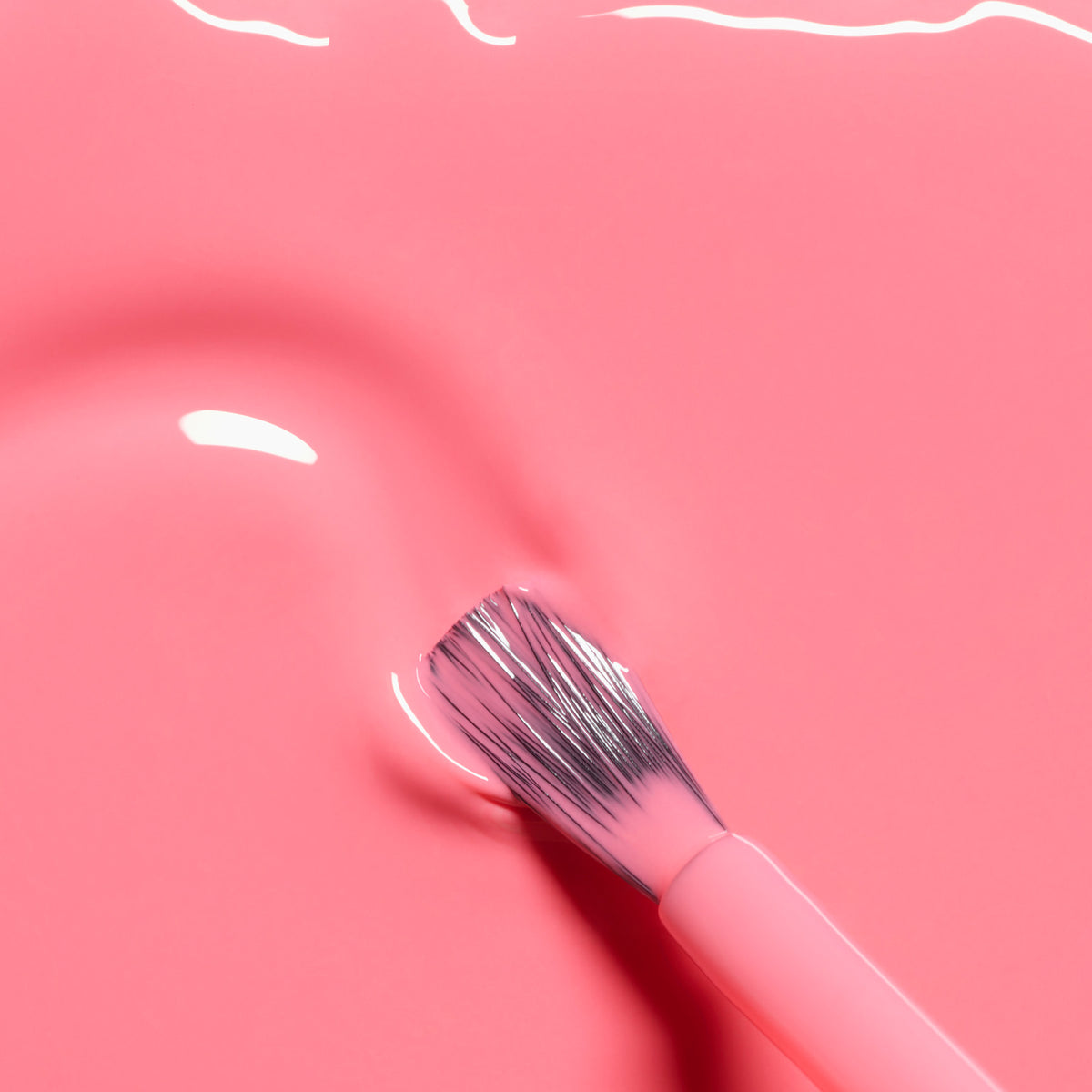 A close-up of a Manucurist Pop nail polish brush resting on a smooth surface coated in vibrant, glossy electric pink polish with bright light reflections.