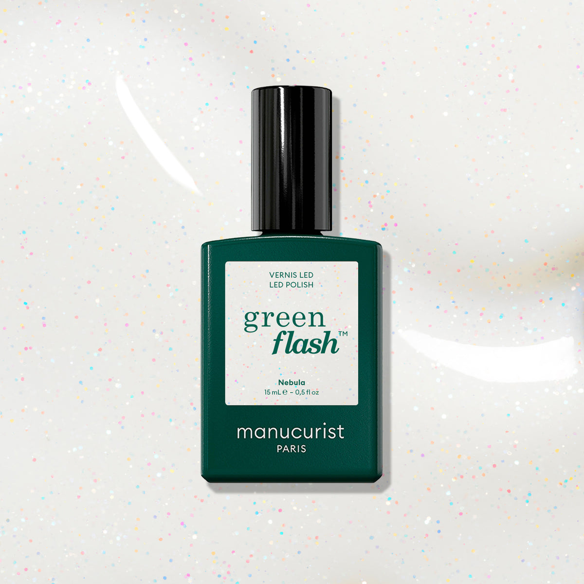 A dark green Manucurist bottle of Green Flash LED polish in shade Nebula is displayed on a white background, showing holographic glitter specks.