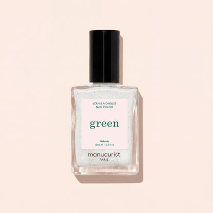 A clear glass bottle of Manucurist nail polish in the shade Nebula, featuring a black cap and white label, is displayed on a pale beige background.