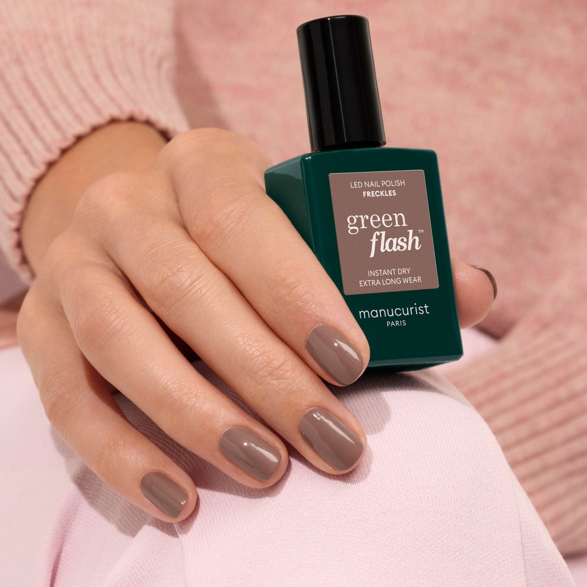 A hand holding a bottle of Manucurist Freckles, a wood-toned brown gel polish.