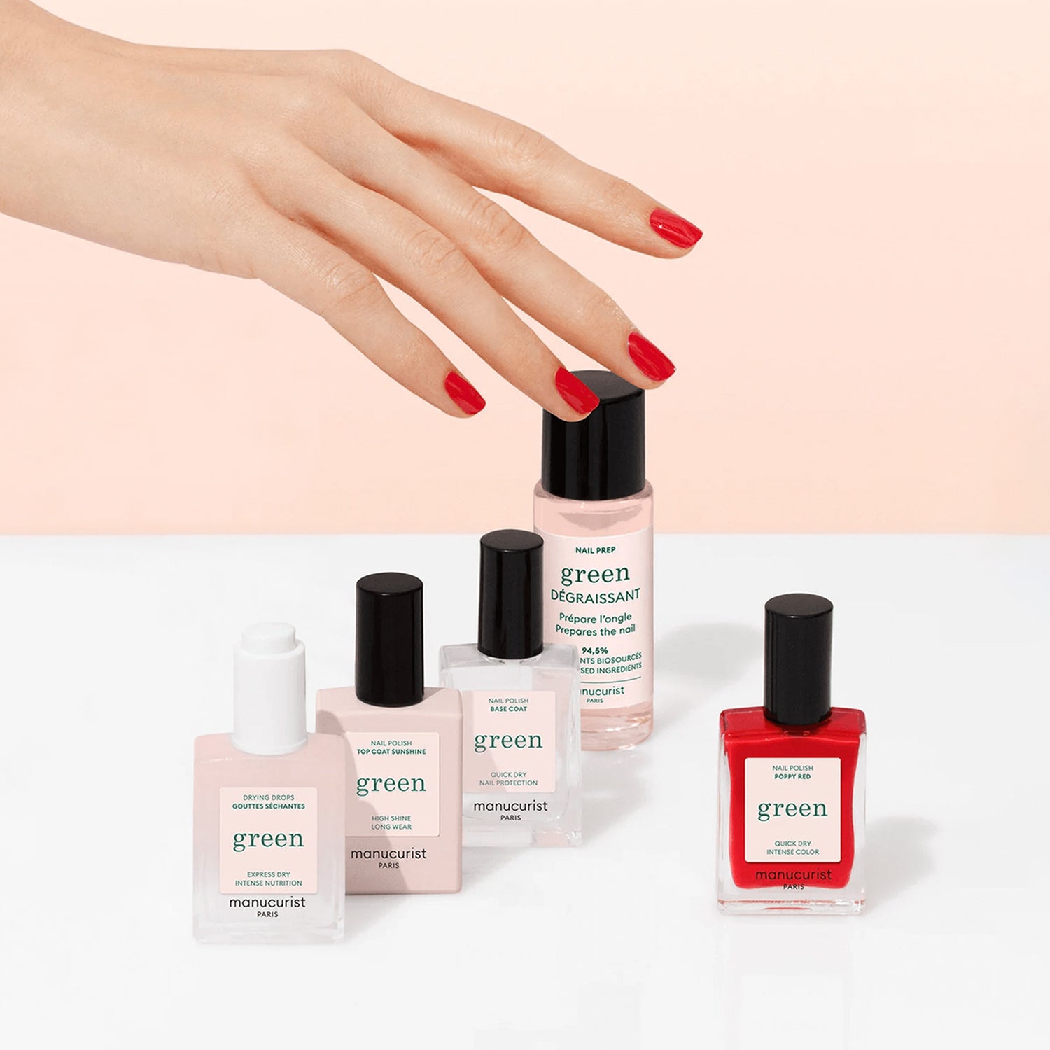 A hand with red nails hovers over five Manucurist Discovery Kit bottles—plant-based nail polish in clear, pink, and red shades—arranged on white with a pink background. Perfect for an eco-friendly manicure.