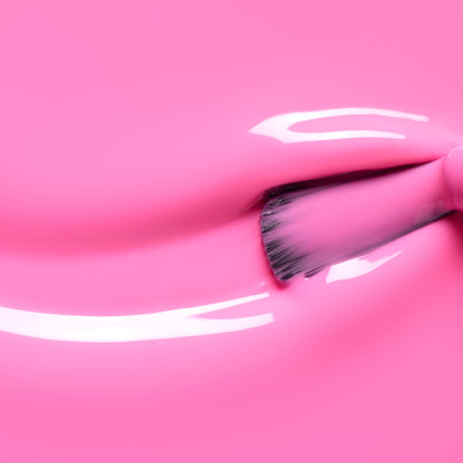 A close-up of a brush applying Bloom by Manucurist—a glossy neon pink polish with subtle blue undertones—creating smooth, shiny streaks on a matching surface from the Green™ range.