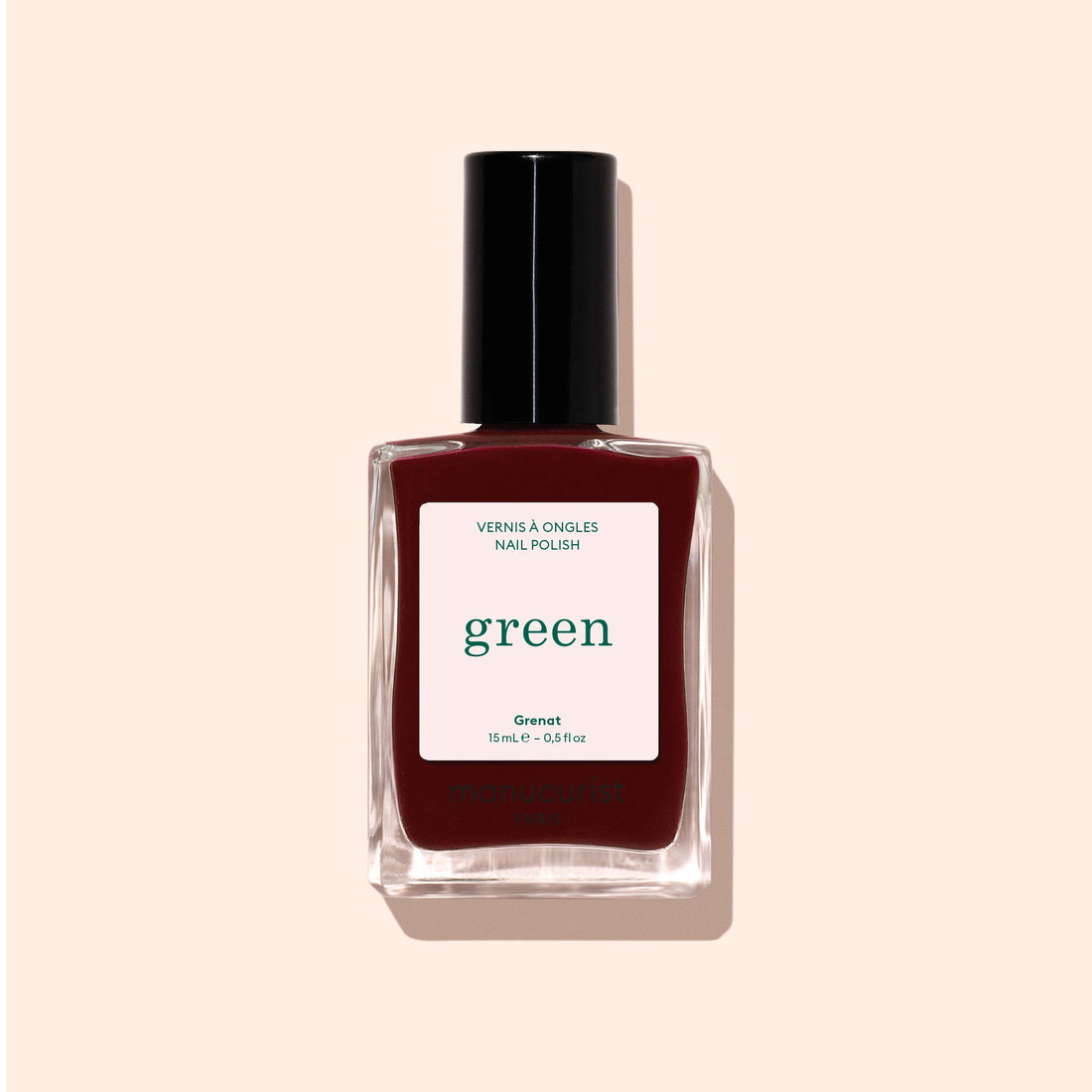 A bottle of Manucurist Grenat red nail polish with a black cap, labeled green and Green™, sits on a light beige background.