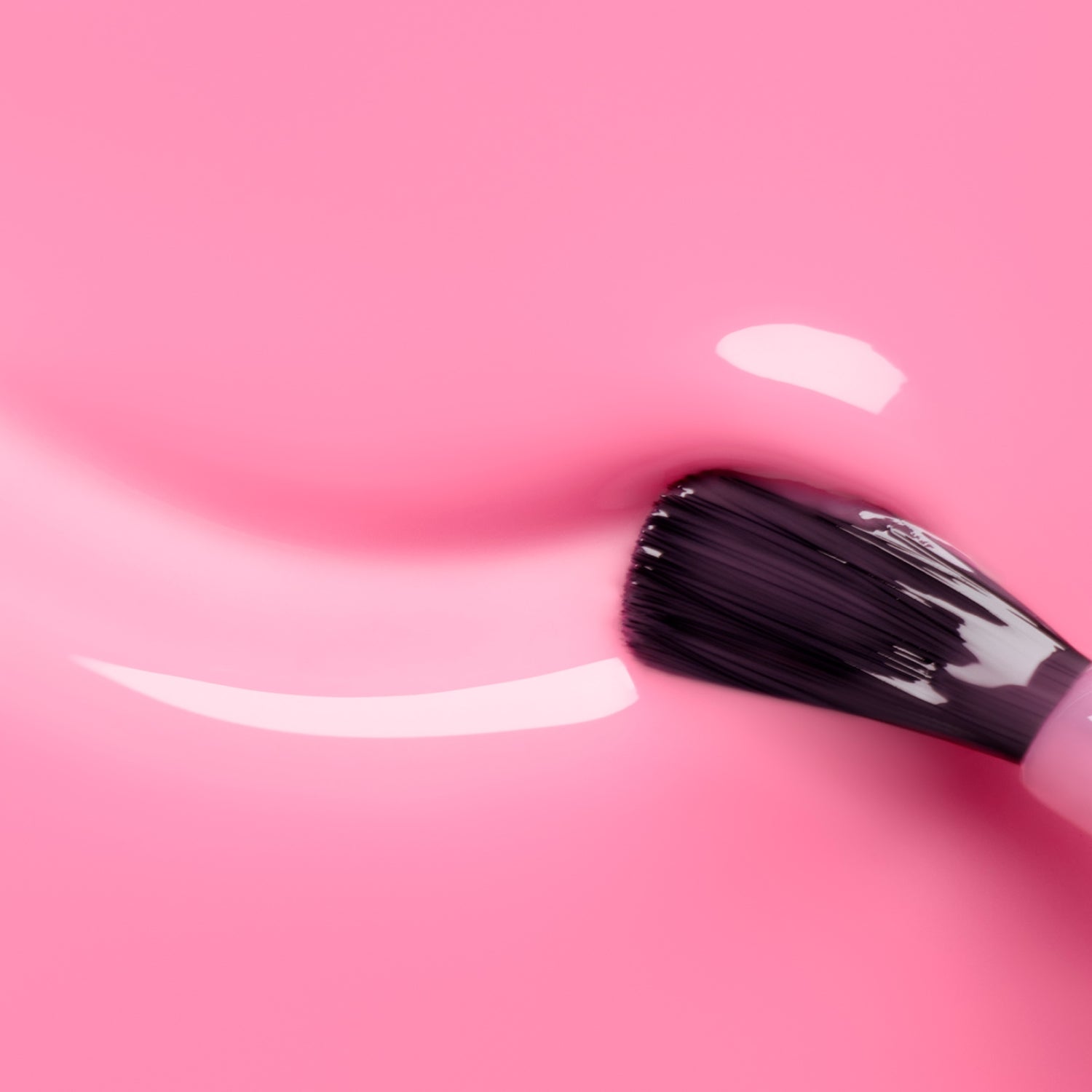 A close-up of a brush applying Manucurist Pink Sorbet Jelly, a translucent pink nail polish, on a smooth pink surface, with reflections showcasing its shiny texture.
