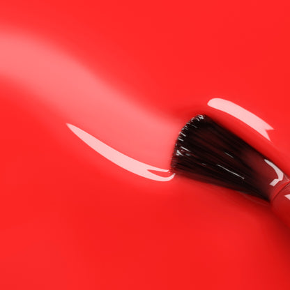 A close-up of a Manucurist Twizzle makeup brush applying a smooth, ultra-glossy streak of polish on a shiny red surface.