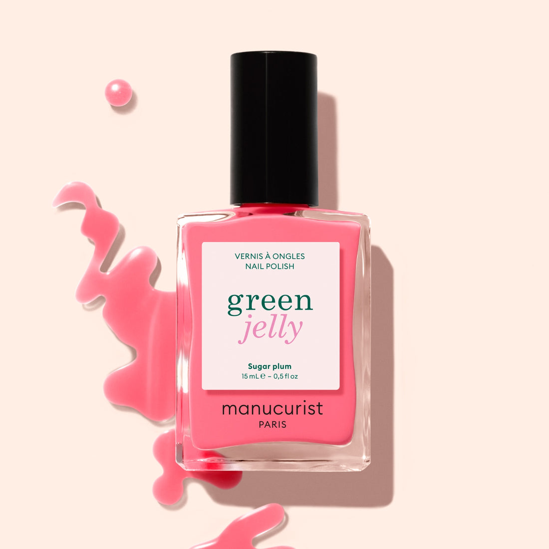 A bottle of Manucurist Sugar Plum Jelly nail polish with translucent pink polish spilled artistically on a light background.