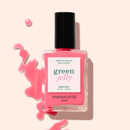 A bottle of Manucurist Sugar Plum Jelly nail polish with translucent pink polish spilled artistically on a light background.