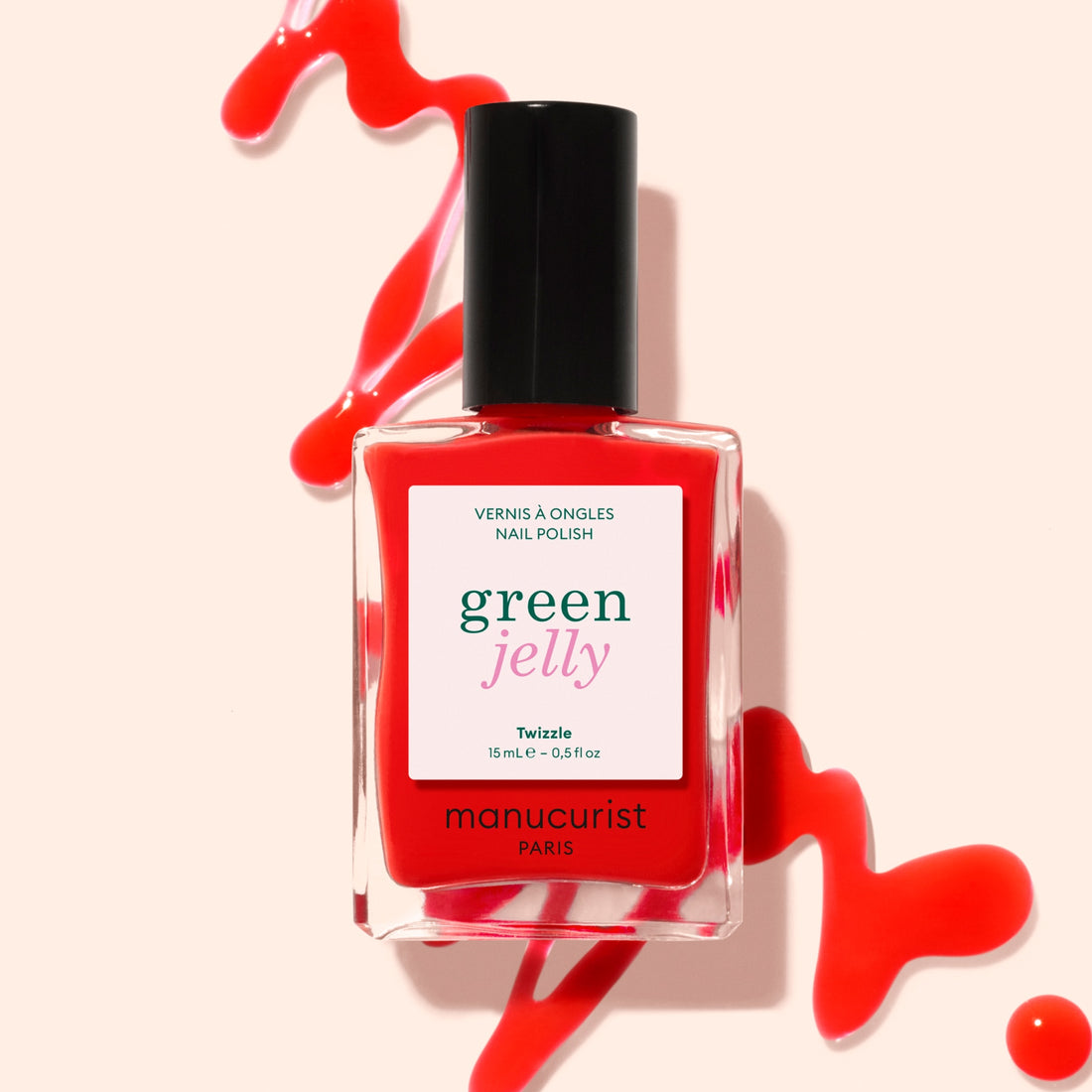 A bottle of Manucurist Twizzle Jelly nail polish in bright, translucent red lies on a light background, with long-lasting polish artistically spilled around it.