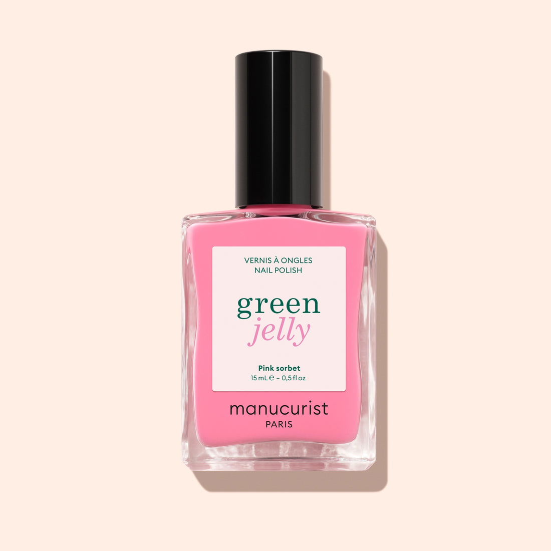 A bottle of Manucurist Pink Sorbet Jelly nail polish with translucent pink liquid, a black cap, and a white label with green and pink text sits against a soft beige background.