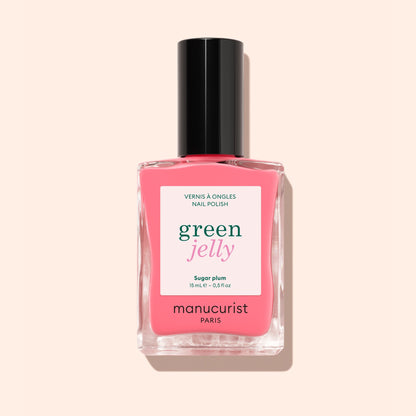 A bottle of Manucurist Sugar Plum nail polish, featuring a translucent pop pink shade with an ultra-glossy finish and a black cap, is shown against a pale pink background.