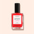 A bottle of ultra-glossy, bright red nail polish labeled Twizzle by Manucurist, with a black cap and white label, set against a pale peach background.