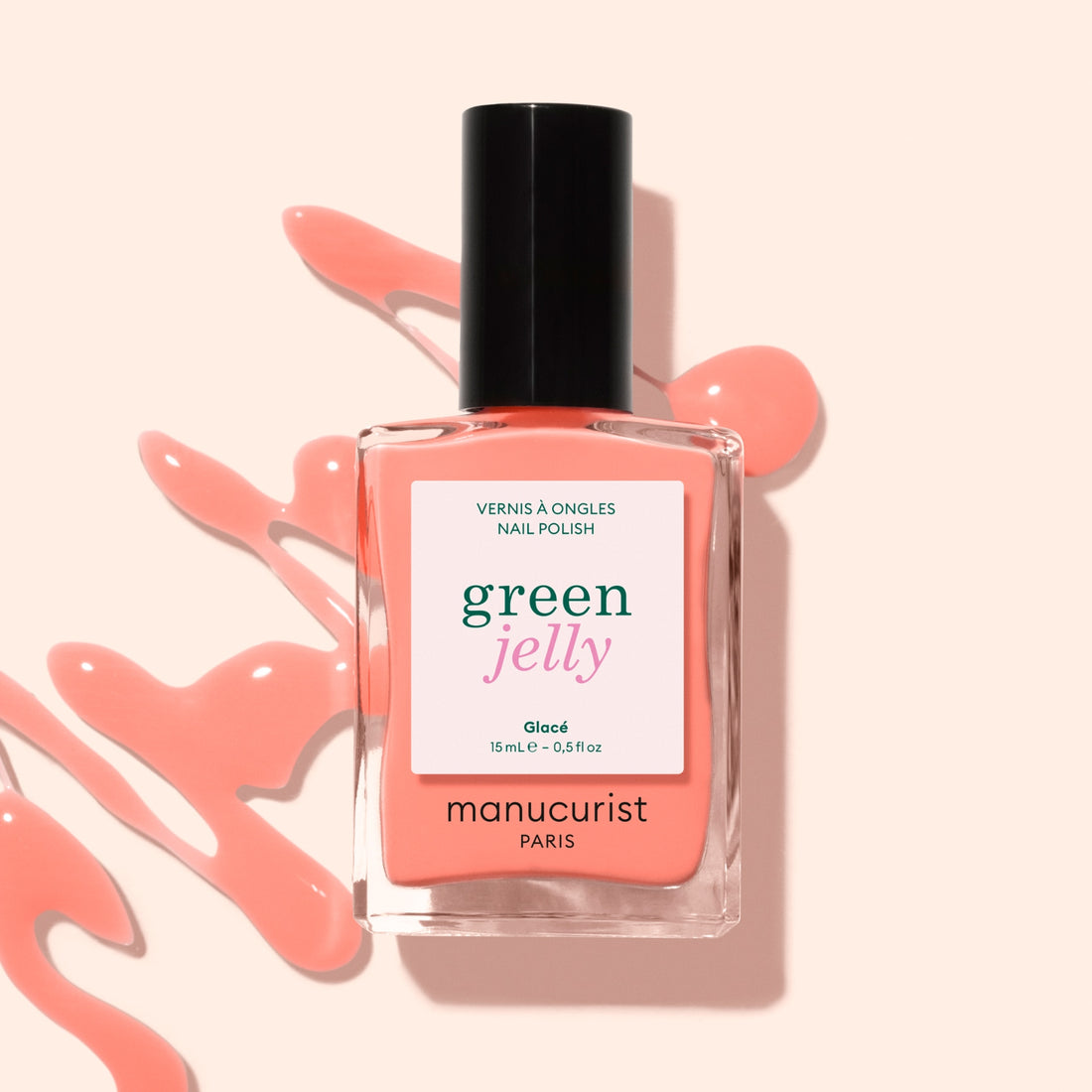 A bottle of Manucurist Glacé Jelly nail polish in a peach-pink shade, with matching ultra-glossy polish artistically splattered on a light pink background.