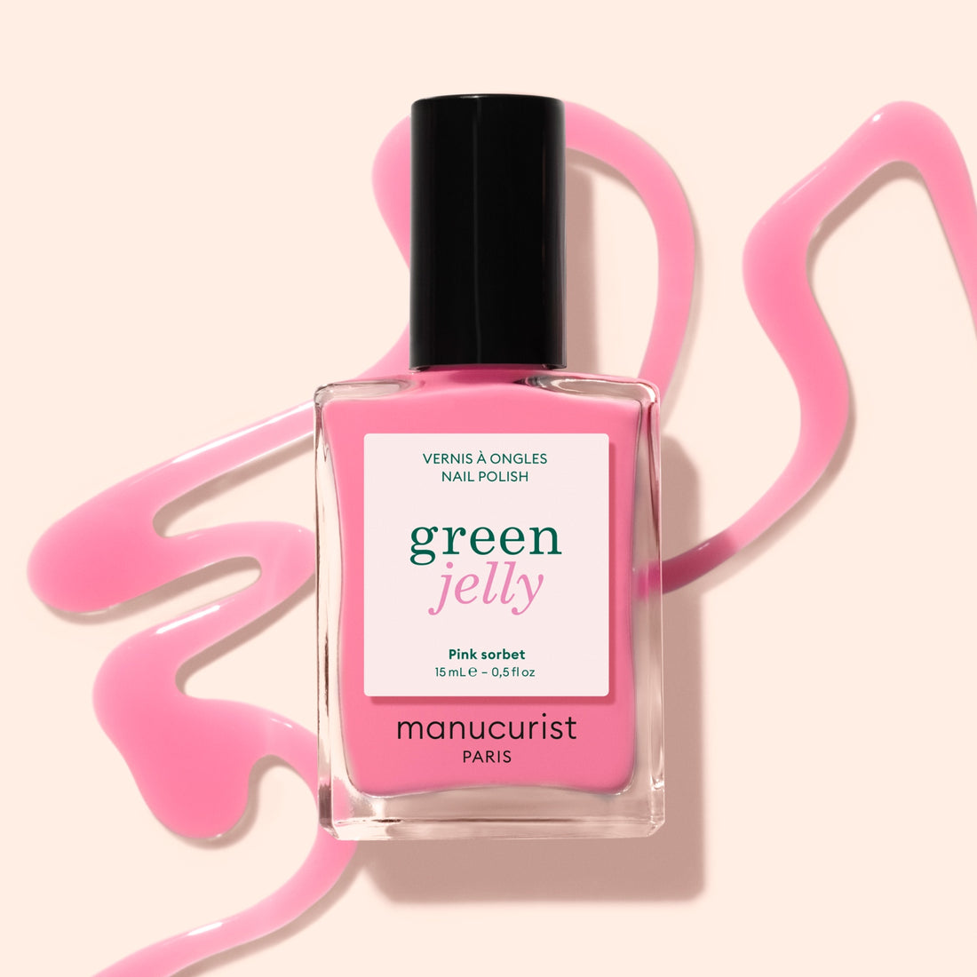 A bottle of Manucurist Pink Sorbet Jelly nail polish stands on a beige surface, surrounded by swirling translucent pink polish.