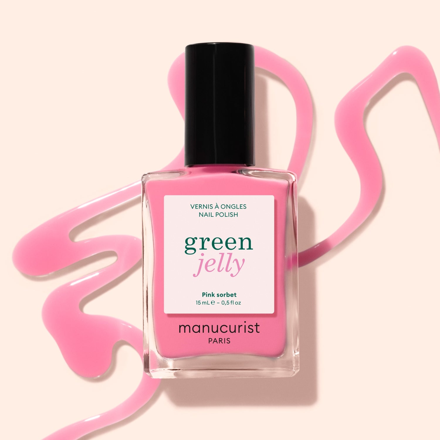A bottle of Manucurist Pink Sorbet Jelly nail polish stands on a beige surface, surrounded by swirling translucent pink polish.