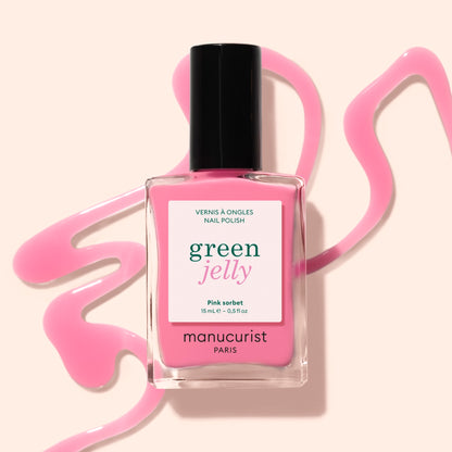A bottle of Manucurist Pink Sorbet Jelly nail polish stands on a beige surface, surrounded by swirling translucent pink polish.
